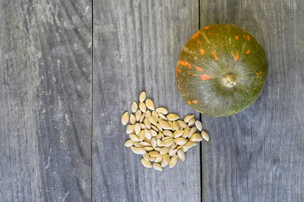 Citrouille est vert-orange et ses graines sont empilées dans une pile sur un fond rustique vintage en bois — Photo