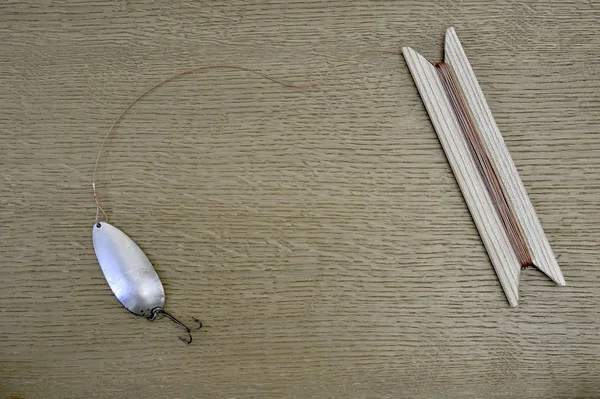 Spinner cuchara casera con un cordón atado a ella y la herida en un carrete de madera. Antiguo concepto de captura de peces depredadores . — Foto de Stock