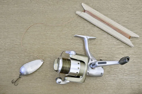 A modern spinning reel with a fishing line and a homemade spoon with a cord tied to it, wound on a wooden reel.