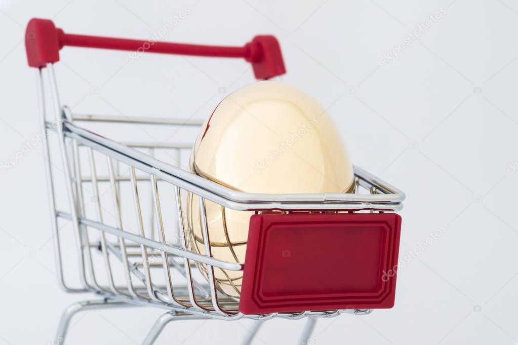 A Golden egg made of metal in a supermarket grocery cart on a light gray background. The concept of a unique offer for the client. Copy space.