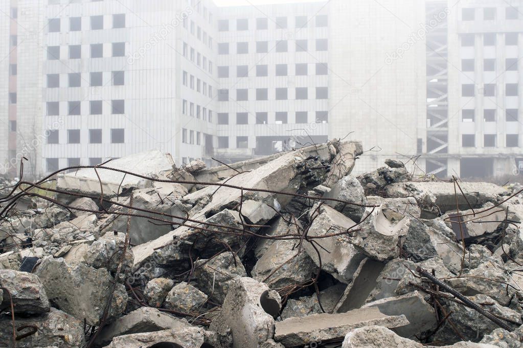 The remains of the destroyed building in the form of piles and a blockage of a pile of stones on the background of a high destroyed structure in a foggy haze. The impact of the destruction. Background