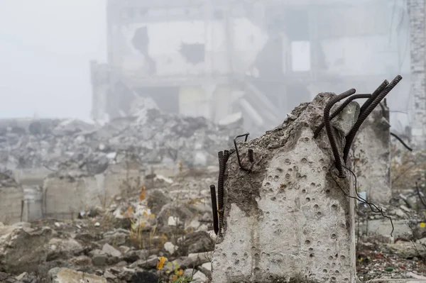 The remains of the destroyed Foundation of the building in the form of piles and rubble from a pile of concrete fragments of stones on the background of the destroyed structure in a foggy haze.