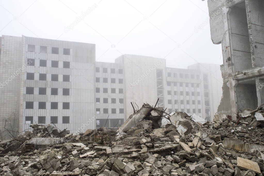 The remains of concrete fragments of gray stones on the background of the destroyed building in a foggy haze.