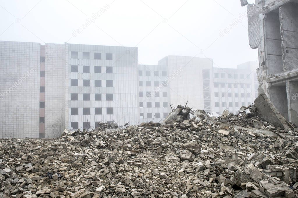 The remains of concrete fragments of gray stones on the background of the destroyed building in a foggy haze.