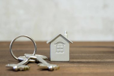 Ev gri kahverengi ahşap ve bulanık beton kombine bir arka plan üzerinde iki metal tuşlarıyla sembolüdür. Gayrimenkul satışı mülkiyet transferi ile teklif kavramı.