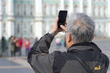 Bir adam turist Asya görünüm Smartphone'da Palace square St. Petersburg üzerinde Rusya, Eylül 2018 bina Hermitage fotoğraf arşivi.