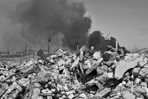 Ein Haufen Betonschutt mit auskragenden Bewehrungsstäben vor dem Hintergrund dicken schwarzen Rauchs am Himmel. Hintergrund. Schwarz-Weiß-Bild — Stockfoto