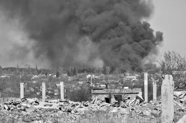 En hög med betong spillror med utskjutande arme rad på bakgrunden av tjock svart rök i den blå himlen. Bakgrund. Svartvit bild — Stockfoto