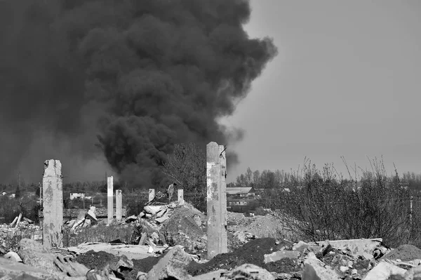 Een stapel betonnen puin met uitstekende wapening op de achtergrond van dikke zwarte rook in de blauwe lucht. Achtergrond. Zwart-wit beeld — Stockfoto