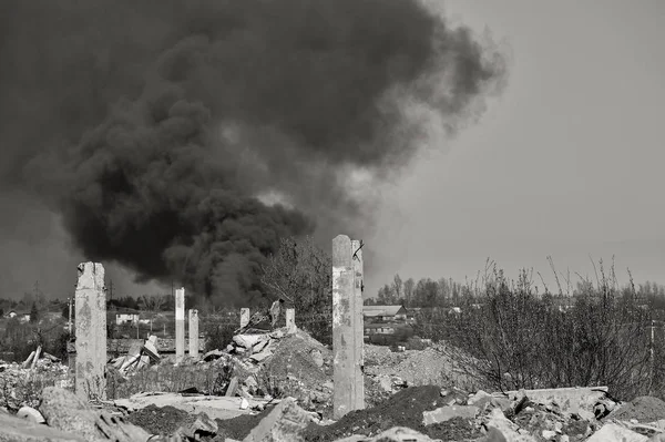 En hög med betong spillror med utskjutande arme rad på bakgrunden av tjock svart rök i den blå himlen. Bakgrund. Svartvit bild — Stockfoto