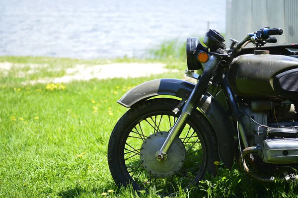 The Soviet Dnepr motorcycle on the green grass of the front part close up against a sandy shore by the lake — Stock Photo, Image