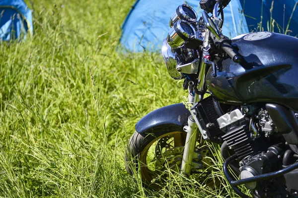 Motocykl černý na zelené trávě na pozadí modrého stanu. Pohled ze strany — Stock fotografie