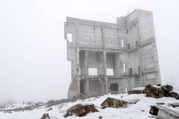 Kar ile kaplı, ön planda yapının parçaları ile sisli bir pus bir beton binanın kalıntıları.
