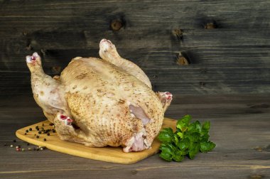 Büyük bir çiğ tavuk ahşap vintage koyu arka plan üzerinde biber bezelye ve kereviz dalı ile bir doğrama Kurulu yatıyor.