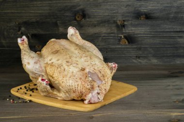 Büyük bir çiğ tavuk ahşap rustik koyu arka plan üzerinde biber bezelye ile bir doğrama Kurulu yatıyor.