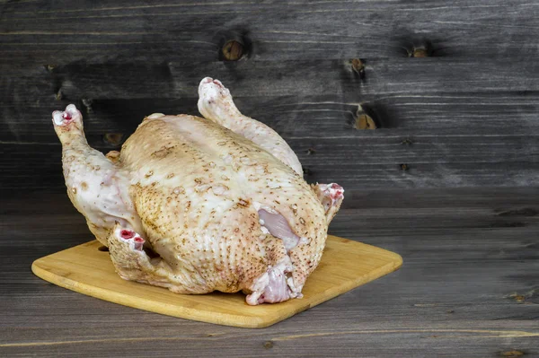 Büyük bir çiğ tavuk ahşap rustik koyu arka plan üzerinde bir bambu kesme Kurulu yatıyor. Alanı, metin için alanı kopyalama