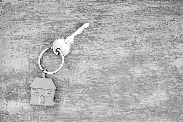 El símbolo de una casa de metal con una llave sobre un fondo gris de hormigón rayado. Blanco y negro . —  Fotos de Stock