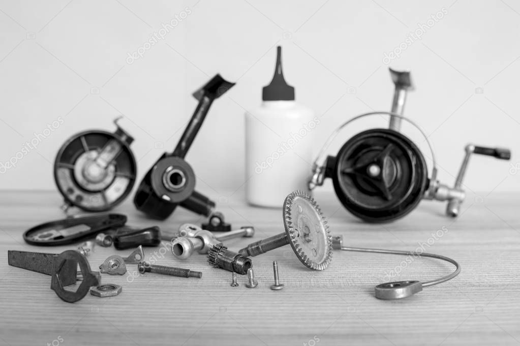 A fishing spinning reel as a whole and a second similar completely disassembled. Black and white image.