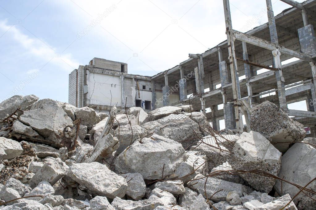 Concrete gray debris close-up on the background of the remains of the destroyed building against the sky. Background