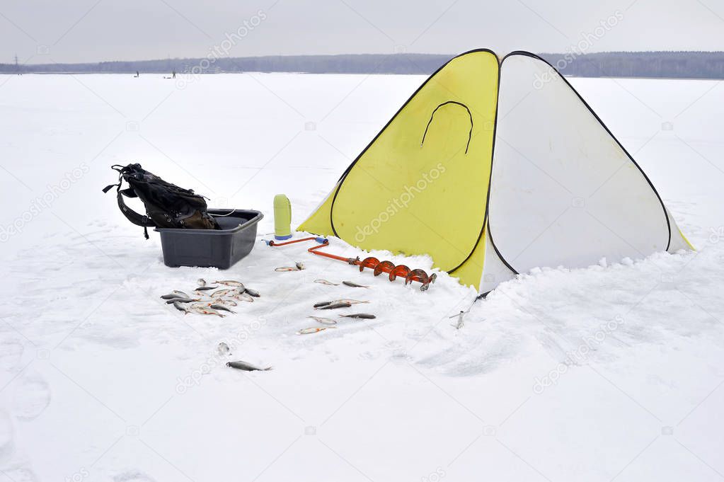 Winter fishing place with a yellow tent and the necessary attributes for fishing.
