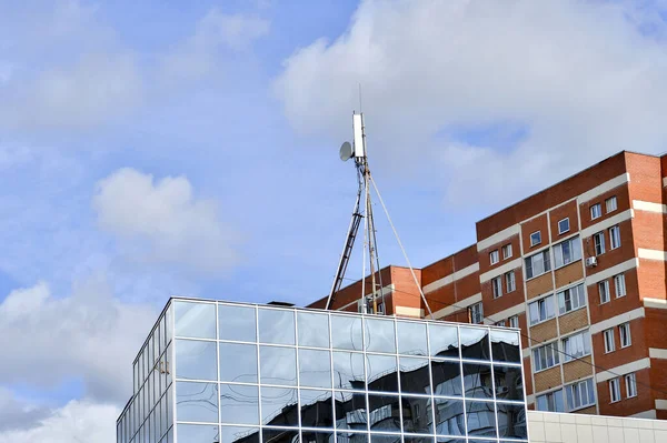 Antennas on a metal support on the roof of a modern building on the background of residential buildings and blue sky.