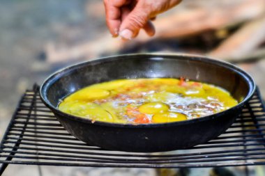Yakın plan yumurtalar, bir kır evindeki açık ateşte kızartma tavasında pişirilir. Çerçevedeki el yemek yaparken tabağı tuzlar. Tabağın ortasındaki sislerde keskinlik.