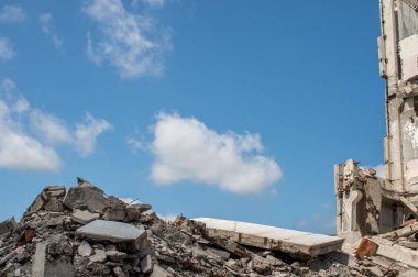 Büyük yıkılmış bir binanın ve mavi gökyüzünün kalıntılarına karşı gri beton enkaz yığını. Arkaplan.
