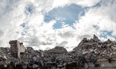 Önünde büyük bir kiriş olan yıkılmış bir binanın beton gri enkazı bulutlu mavi gökyüzüne çarpıyor. Panorama.