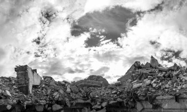 Yıkılmış bir binanın beton gri enkazı ön planda büyük bir kiriş ile bulutlu desenli bir gökyüzünün arka planına çarpıyor..