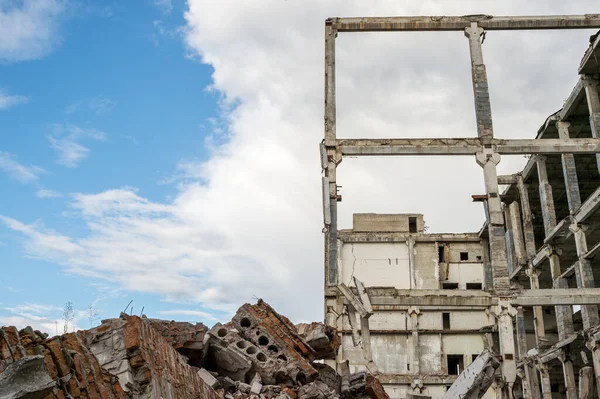 A pile of construction debris and a destroyed frame of a building made of concrete beams against a blue sky. — Stock Photo, Image