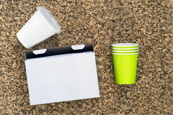 White cardboard box, plastic Cup and paper cups on the background of organic texture of dry petals.