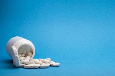 Mavi arka planda dağınık haplarla dolu beyaz bir şişe..