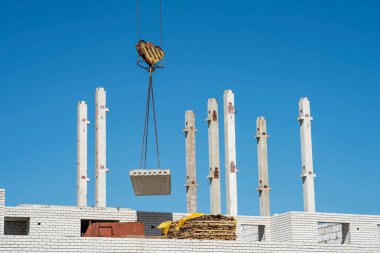 Gökyüzüne doğru uzanan beton kirişlerin arka planında bir tuğla ev inşa edilirken vinç ile beton levha tedariği. Geçmişi. Ceset yok..