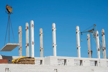 Gökyüzüne doğru uzanan beton kirişlerin arka planında bir tuğla ev inşa edilirken vinç ile beton levha tedariği. Geçmişi. Ceset yok..
