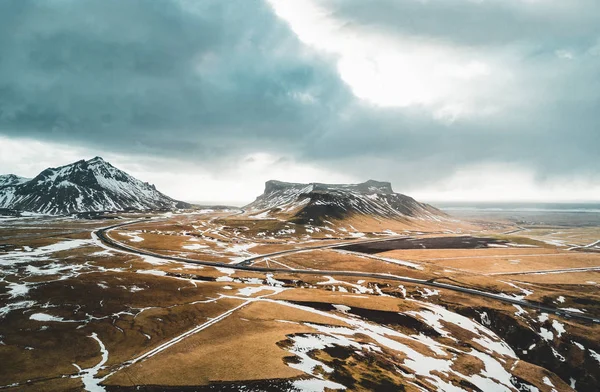 Ісландська пташиного польоту краєвид зі снігом і хмарами, вулиці і жовто-зелені трави — стокове фото