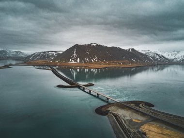 Snaefellsnes yarımadasında deniz üzerinde köprüsü olan İzlanda 'daki 1 no' lu yolun havadan görünüşü bulutlu, su ve dağ manzaralı.