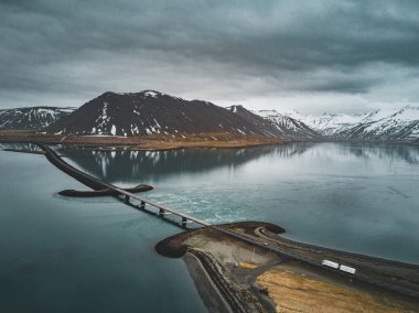 Snaefellsnes yarımadasında deniz üzerinde köprüsü olan İzlanda 'daki 1 no' lu yolun havadan görünüşü bulutlu, su ve dağ manzaralı.