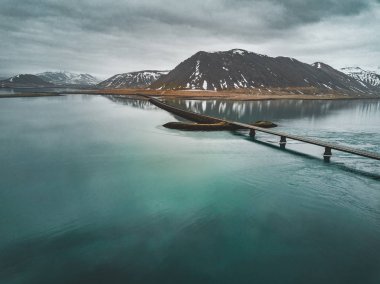 Snaefellsnes yarımadasında deniz üzerinde köprüsü olan İzlanda 'daki 1 no' lu yolun havadan görünüşü bulutlu, su ve dağ manzaralı.