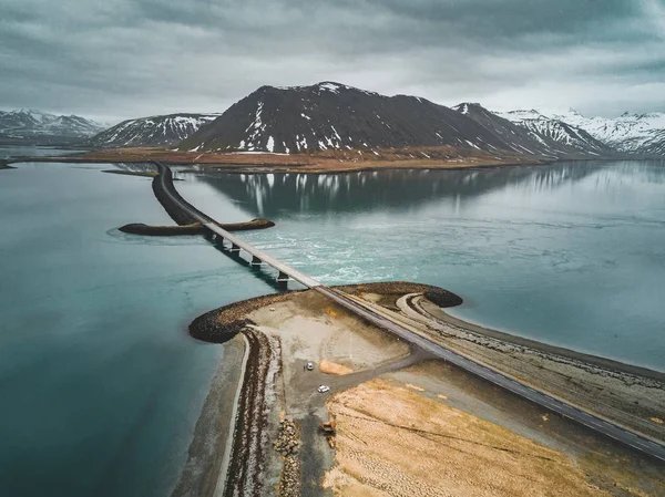 Vista aérea da estrada 1 na Islândia com ponte sobre o mar na península de Snaefellsnes com nuvens, água e montanha no fundo — Fotografia de Stock