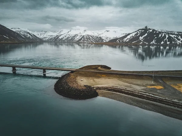 Vista aérea da estrada 1 na Islândia com ponte sobre o mar na península de Snaefellsnes com nuvens, água e montanha no fundo — Fotografia de Stock
