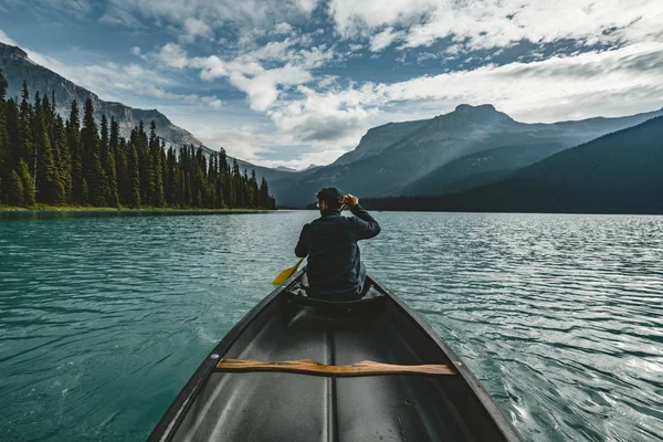 Hombre joven Piragüismo en el lago Esmeralda en las montañas rocosas canada con canoa y montañas en el fondo de agua azul . — Foto de Stock