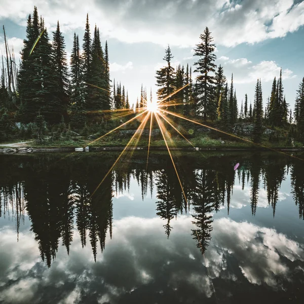 Lac sur le sommet du mont Revelstoke coucher de soleil réflexion étoile de soleil à travers la forêt avec ciel bleu et nuages. Colombie-Britannique Canada . — Photo