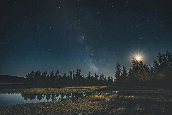 Milky Way galaxy night sky over forest with moon and reflection. Vancouver Island, Tofino, Canada