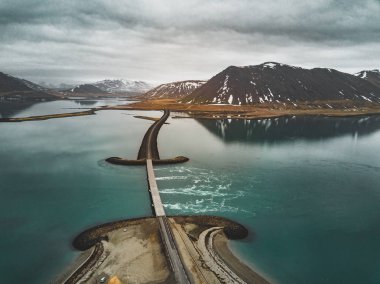 Snaefellsnes yarımadasında deniz üzerinde köprüsü olan İzlanda 'daki 1 no' lu yolun havadan görünüşü bulutlu, su ve dağ manzaralı.