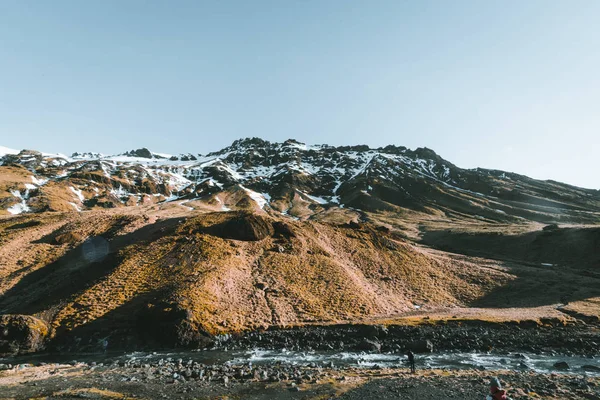 Přírodní koupaliště Seljavallalaug na Islandu s mužem ve vodě a zasněžené počasí a všude kolem hory. Slunečné počasí a modrá obloha. — Stock fotografie
