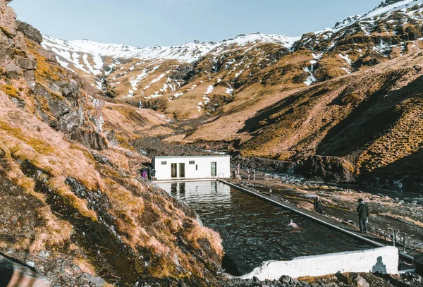 Luonnollinen uima-allas Seljavallalaug Islannissa miehen kanssa vedessä ja luminen sää ja vuoret ympäri. Aurinkoinen sää ja sininen taivas . — kuvapankkivalokuva