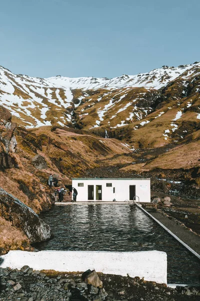 Natuurlijke zwembad Seljavallalaug in IJsland met man in water en snowy weer en de bergen rondom. Zonnig weer en blauwe hemel. — Stockfoto
