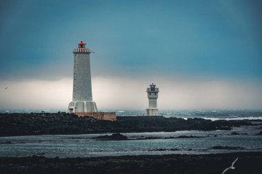 Arkranes beyaz feneri ona su ve taş çevrili yakın iki ev ile İzlanda'daki doğal parlak ışık.
