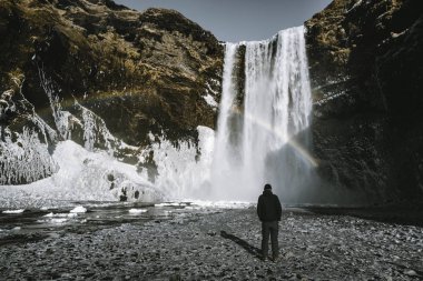 Bir kişi admirnig Skogafoss şelale gökkuşağı ile güzellik İzlanda'yer..