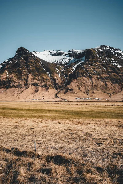 Island typické horské zimní scéna s trávou v popředí a mohutné hory v pozadí. — Stock fotografie